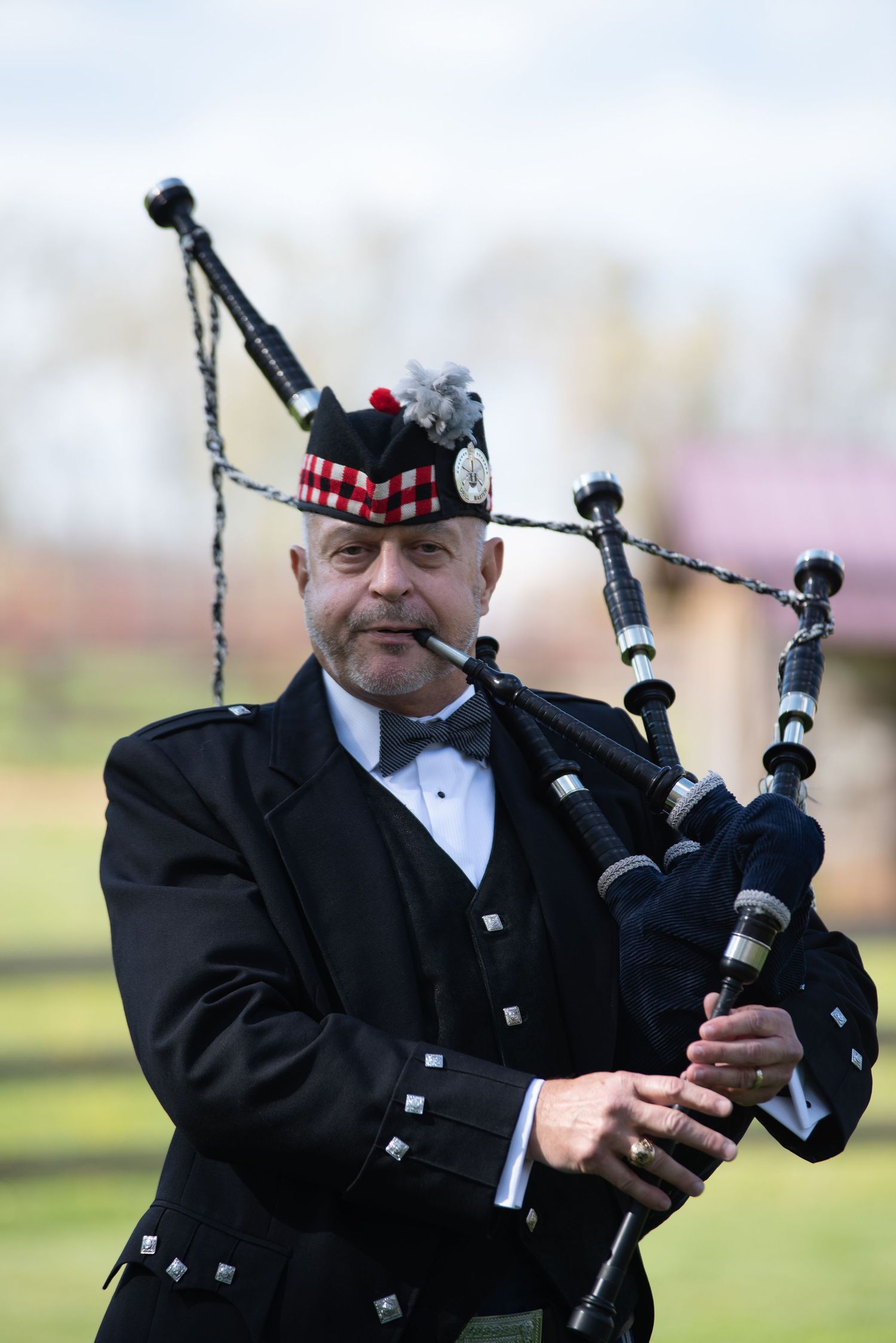 A bagpiper in traditional Scottish attire performs outdoors at a wedding celebration.