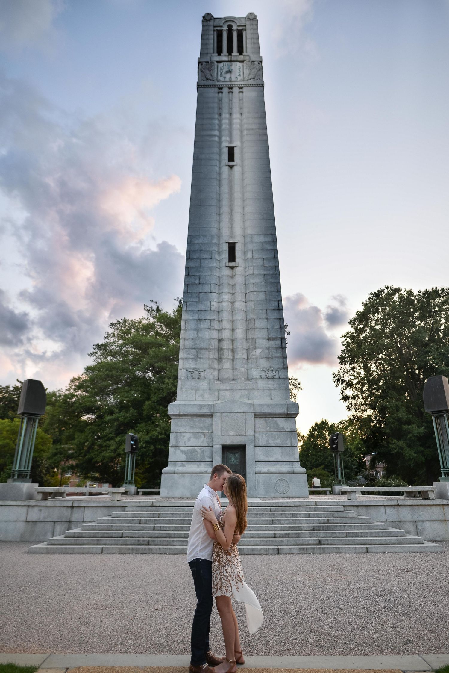 Couple sharing a kiss in front of a tall historic bell tower at sunset during engagement photos.