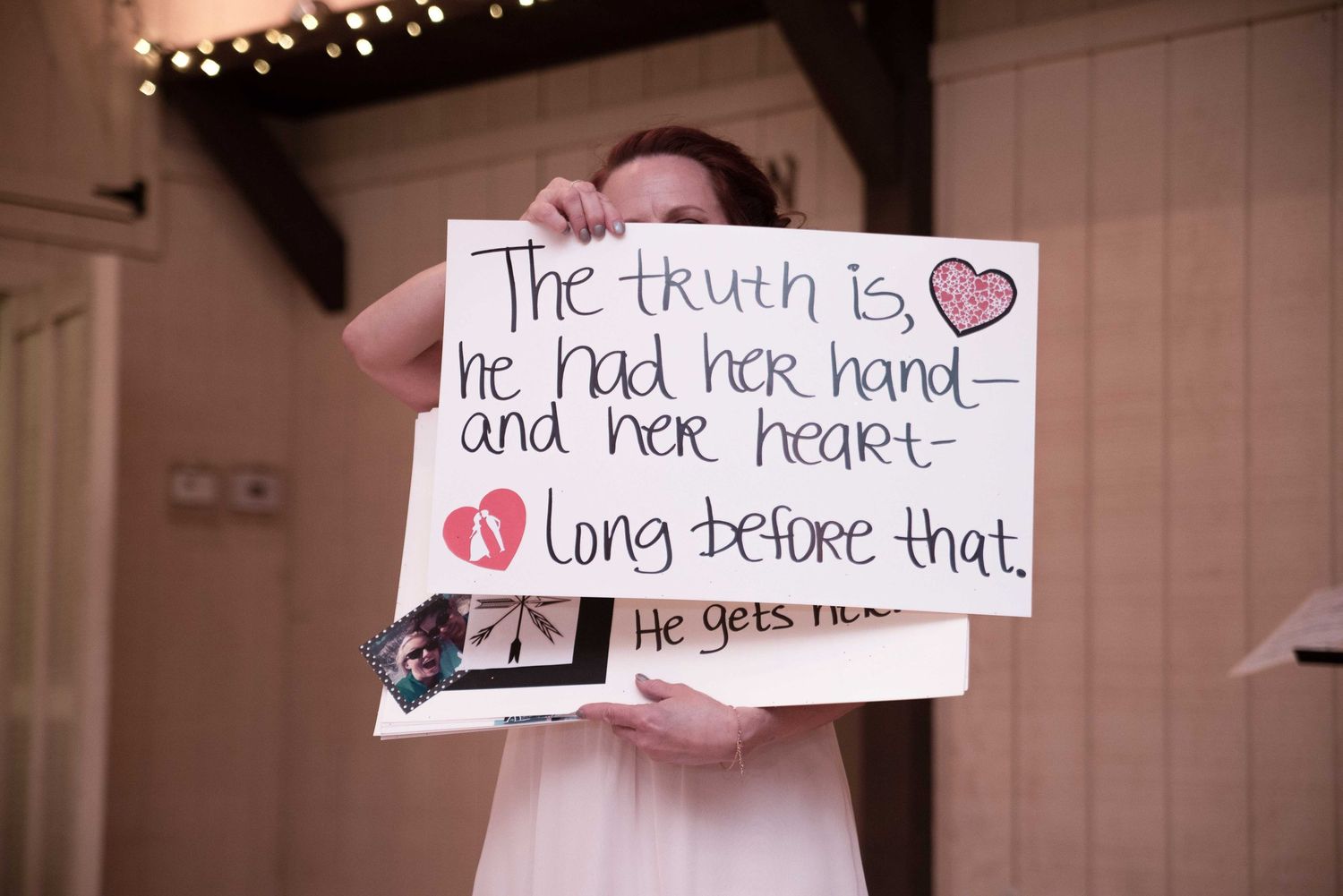 Young flower girl holds handmade wedding sign reading romantic quote about love at indoor wedding ceremony.