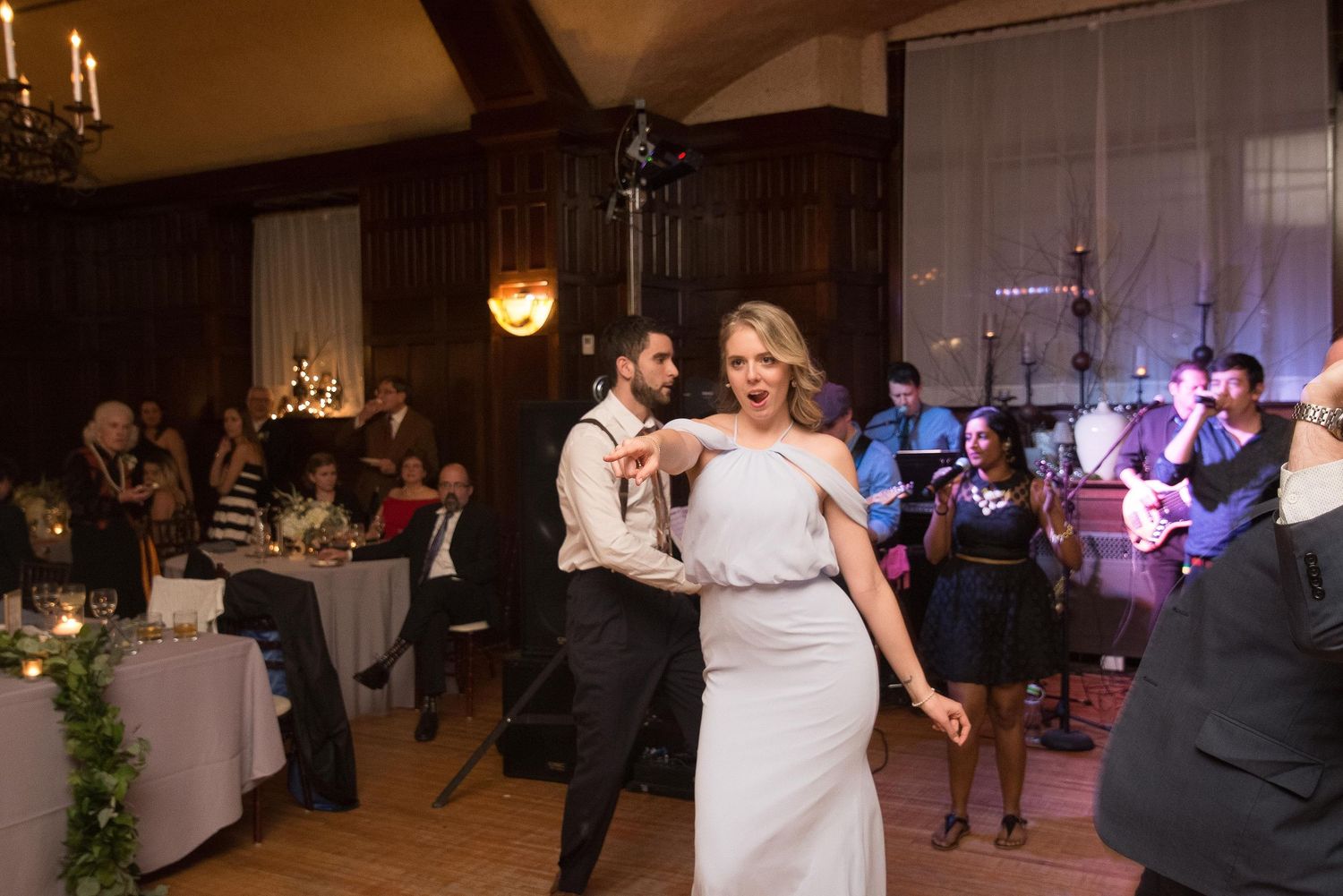 Bride and groom share a joyful first dance at elegant wedding reception with live band performing in background.
