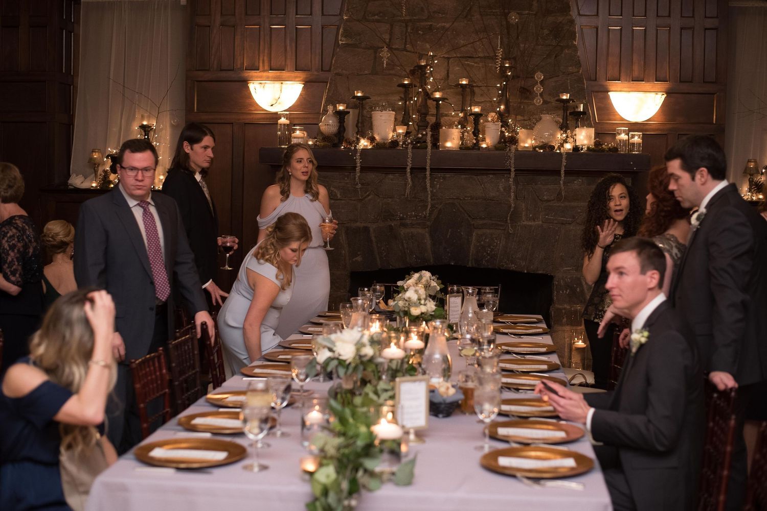 Elegant wedding reception dinner in a grand hall with guests gathered around a long table adorned with floral centerpieces.
