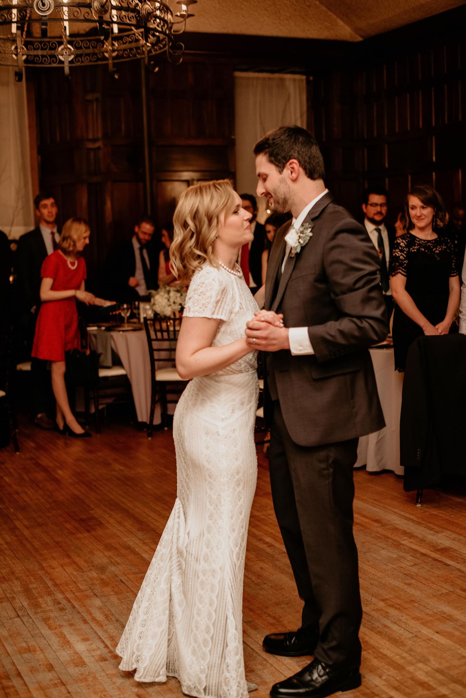 Bride and groom share their first dance at elegant wedding reception, guests watching in warmly lit ballroom.