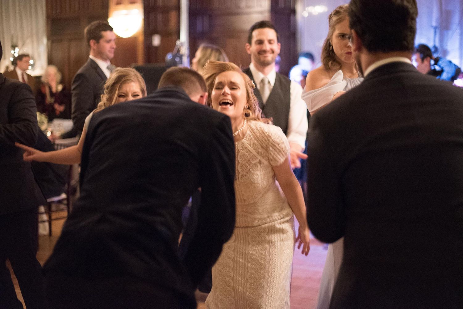 Bride laughing joyfully during wedding reception dance floor celebration with guests in elegant formal attire.