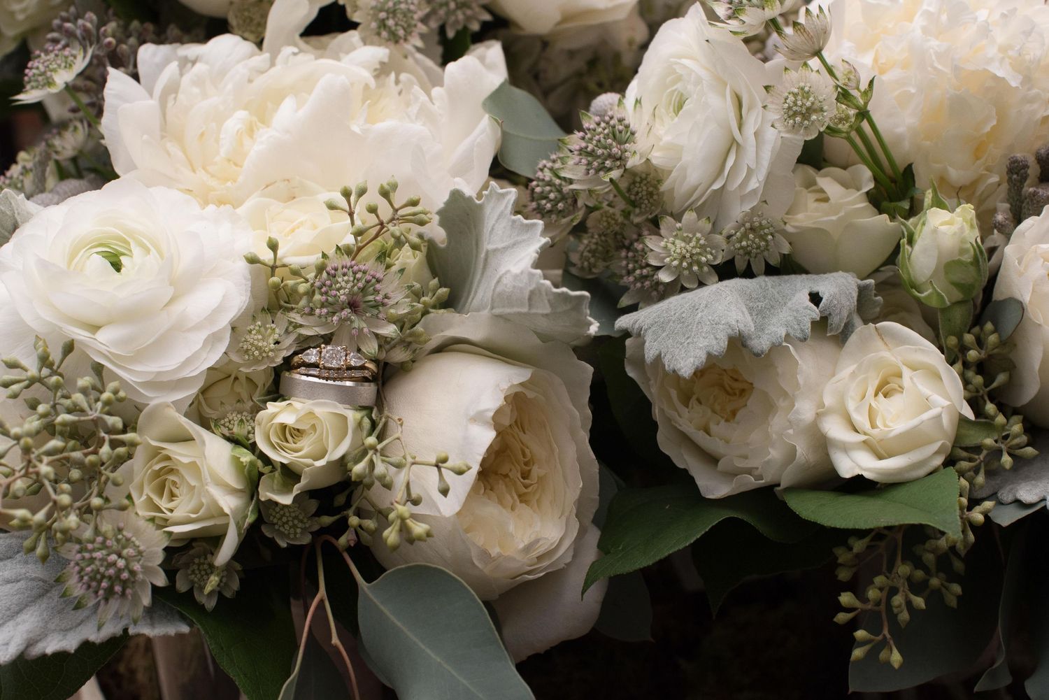 Elegant white wedding bouquet featuring peonies, roses, and ranunculus with eucalyptus accents.