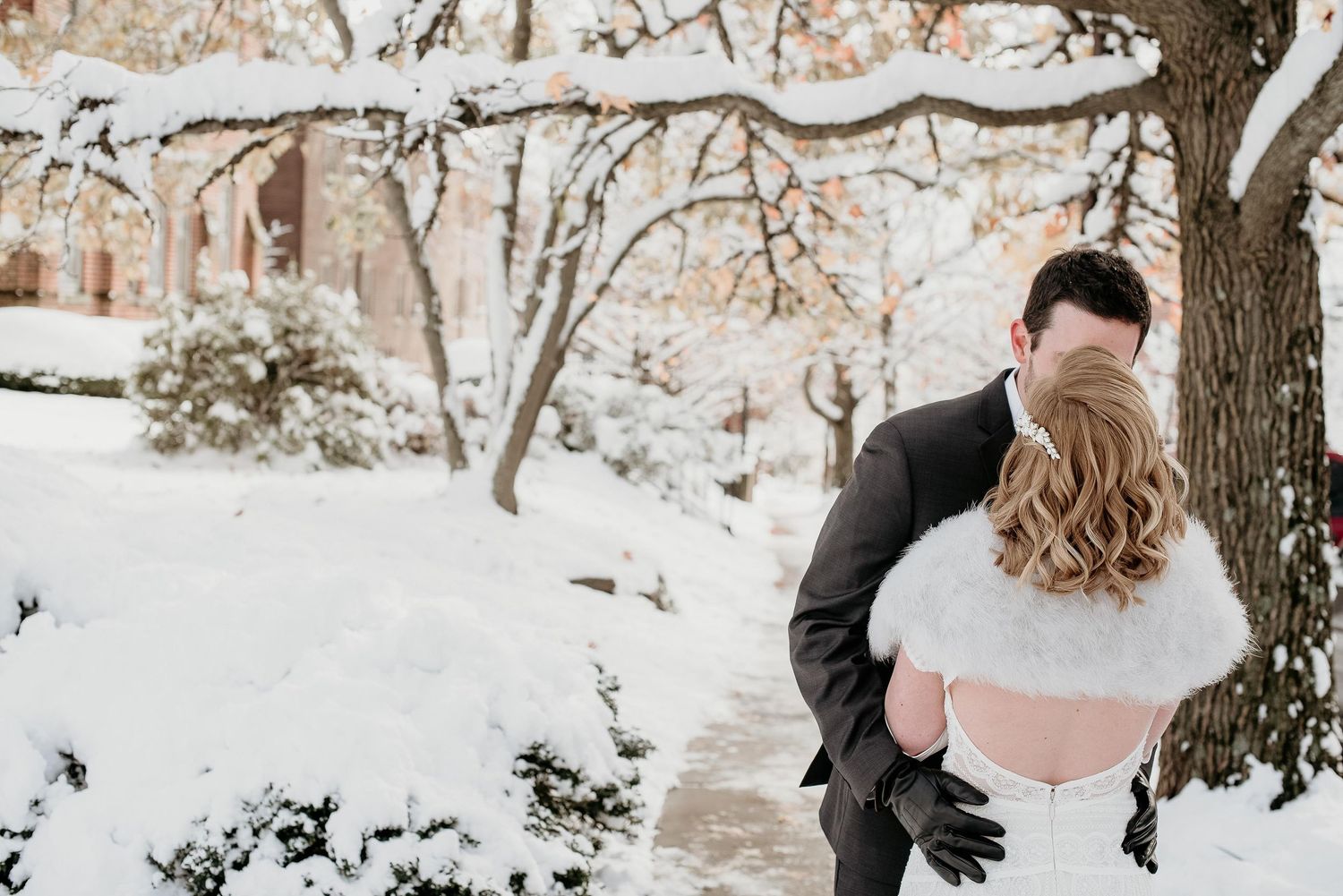 Groom dips bride in white fur shawl for a kiss outdoors in a snow-covered winter wedding setting.