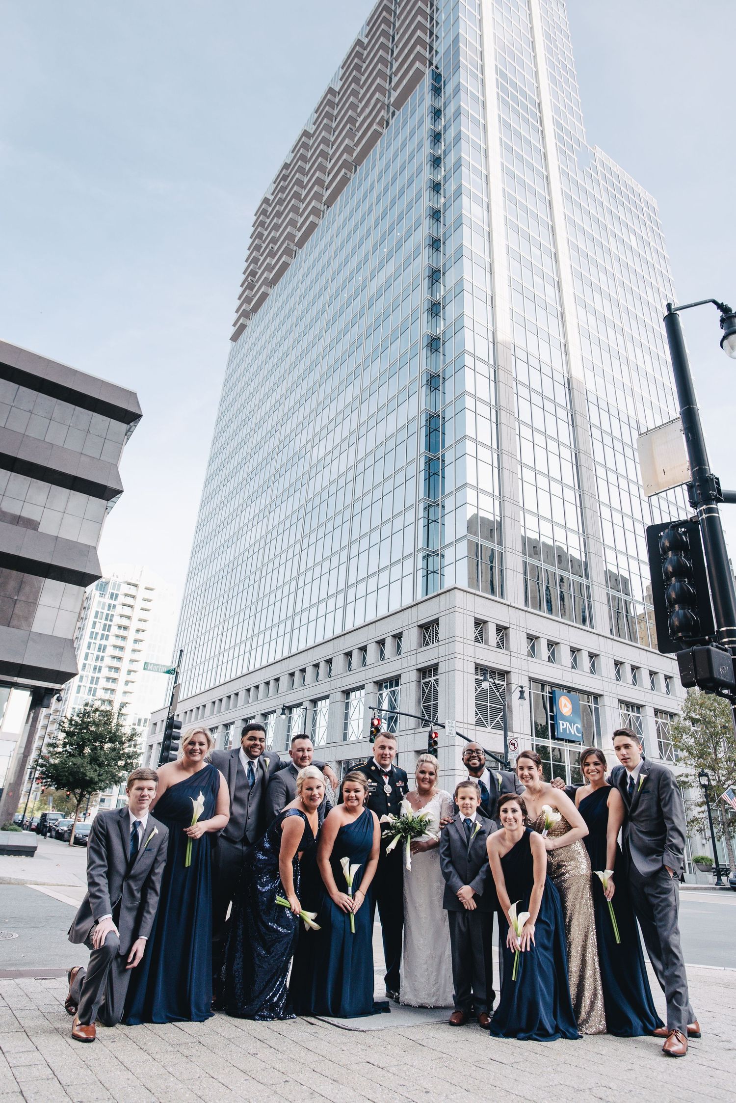 Wedding party posing in navy and gold attire in front of a glass skyscraper downtown.