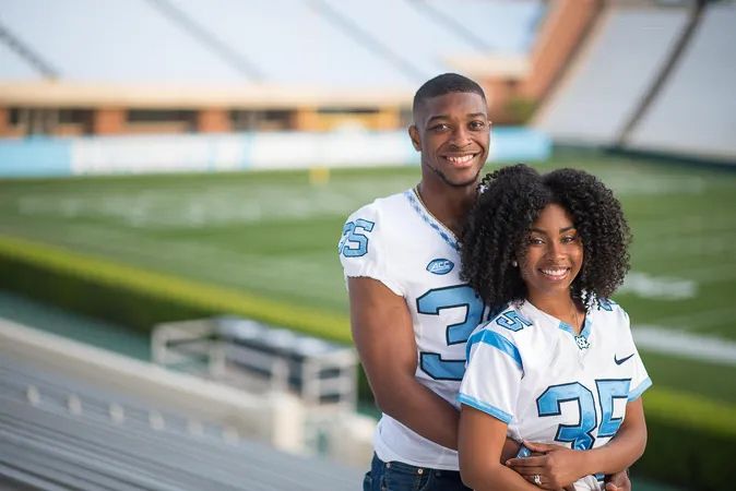A smiling couple poses together in matching football jerseys number 35 at a college stadium.