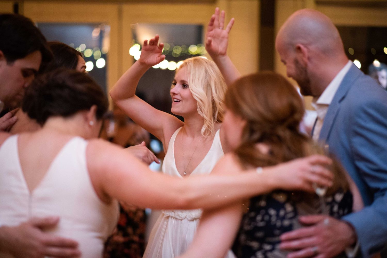 Bride in white dress dancing joyfully with guests at elegant wedding reception celebration.
