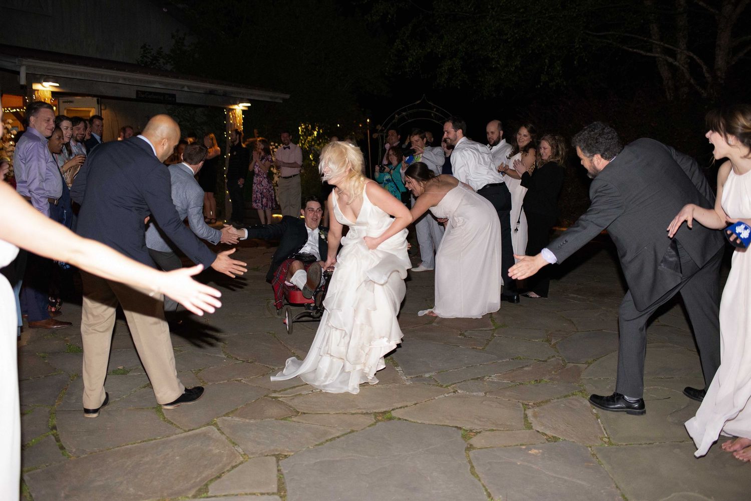 Bride in white gown dancing with guests at outdoor wedding reception at night.