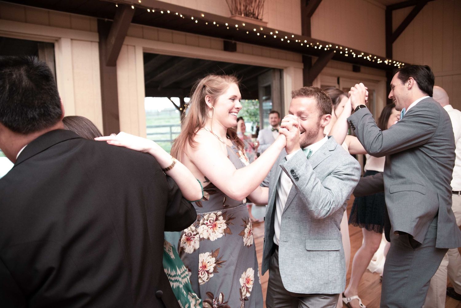 Guests dancing and laughing together at an indoor wedding reception venue with string lights.