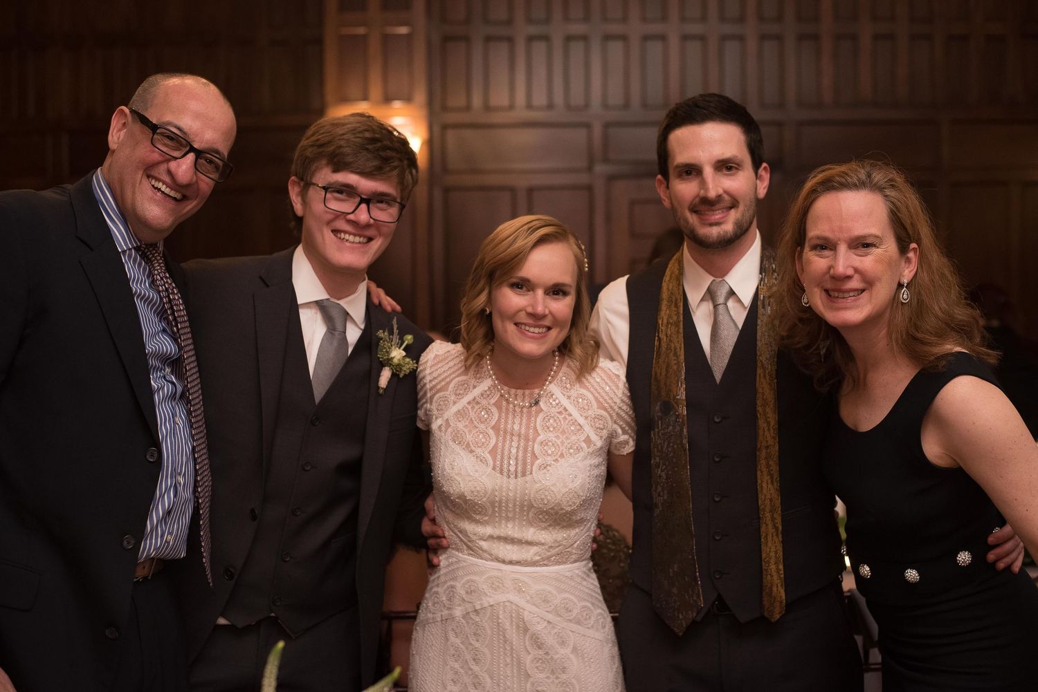 Wedding party of five smiling together, bride in white lace dress flanked by family.
