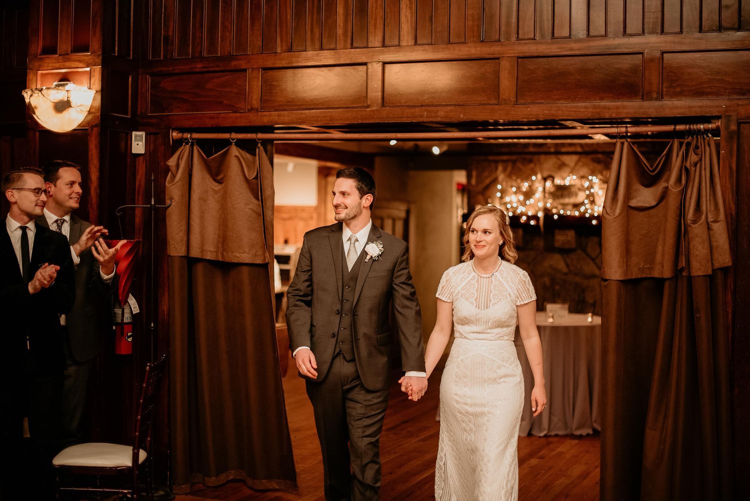 Bride and groom holding hands making grand entrance at elegant wood-paneled wedding reception venue.
