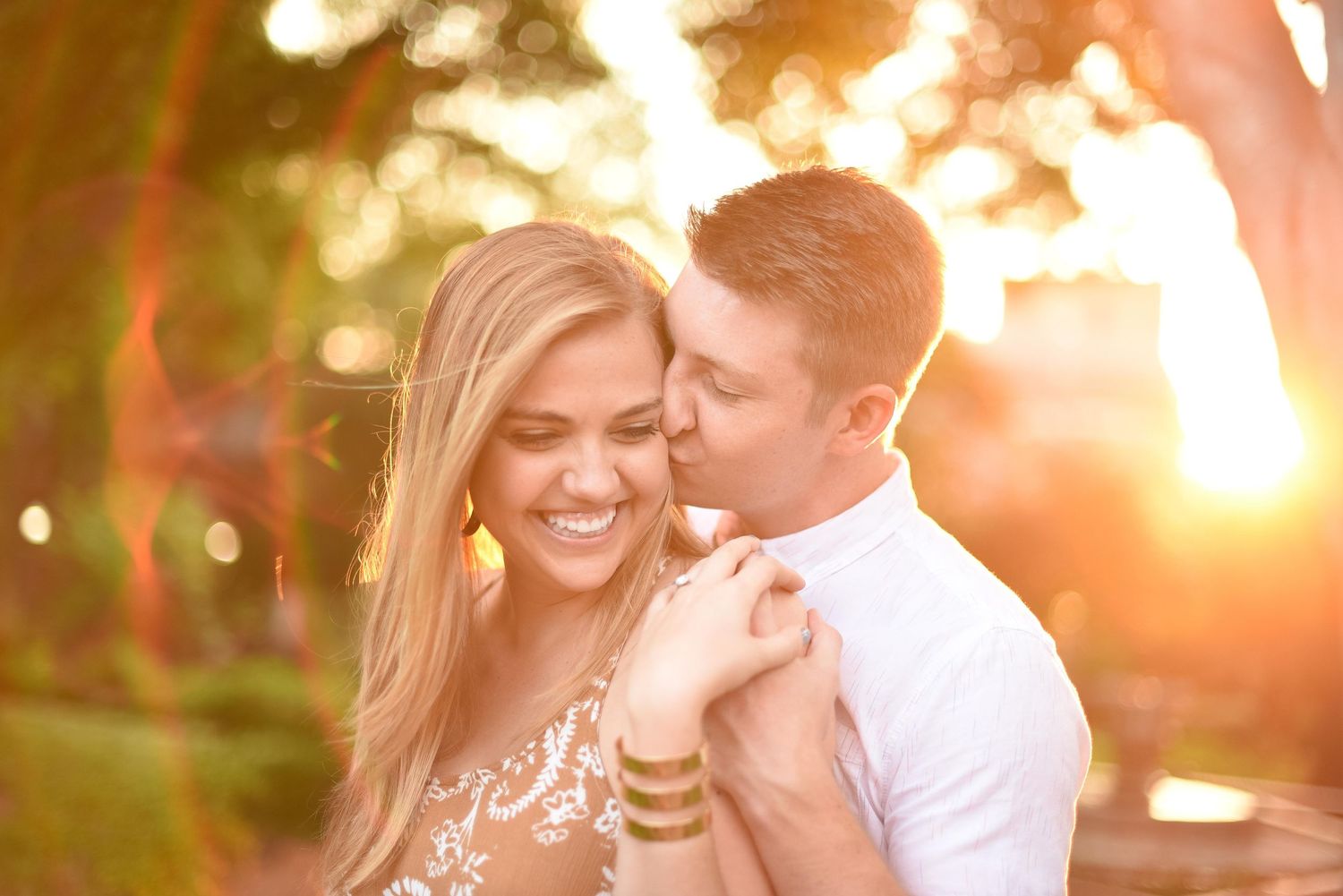 Couple sharing a romantic moment at golden hour, woman smiling as man kisses her cheek outdoors.