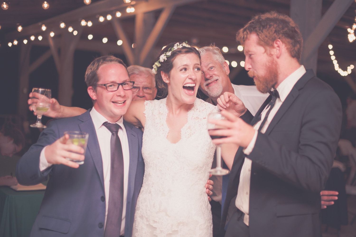 Bride laughing joyfully with wedding guests holding champagne glasses at a festive reception.
