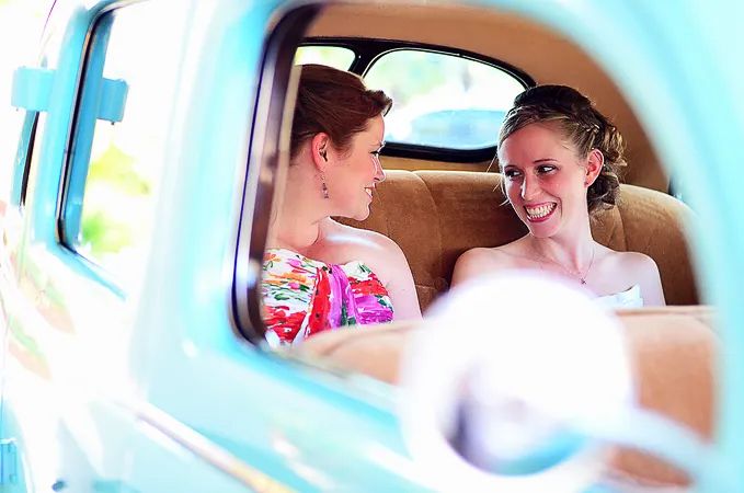 Bride and bridesmaid smiling together inside a vintage turquoise truck window.
