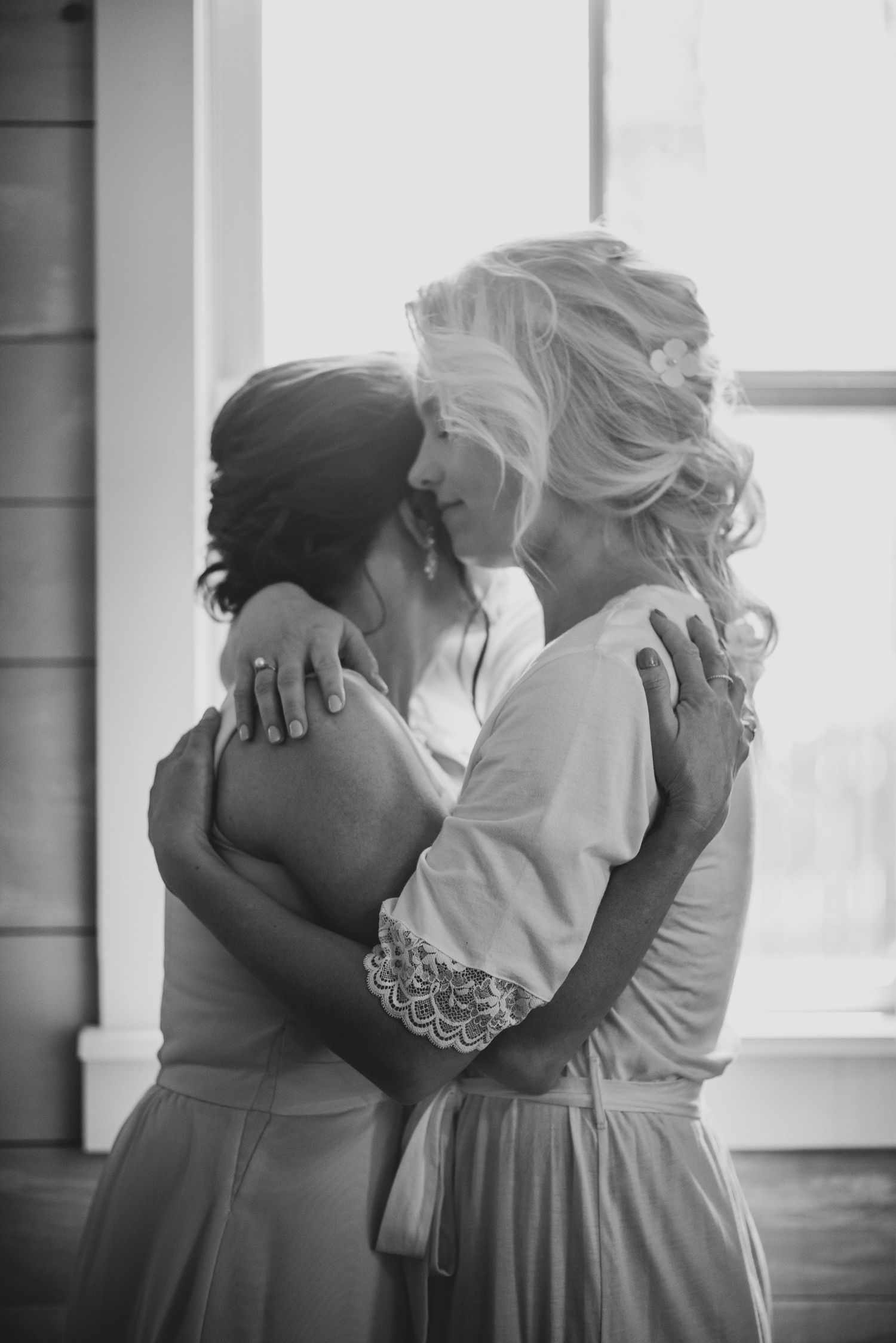 Black and white photo of bride sharing emotional embrace with bridesmaid before wedding ceremony.