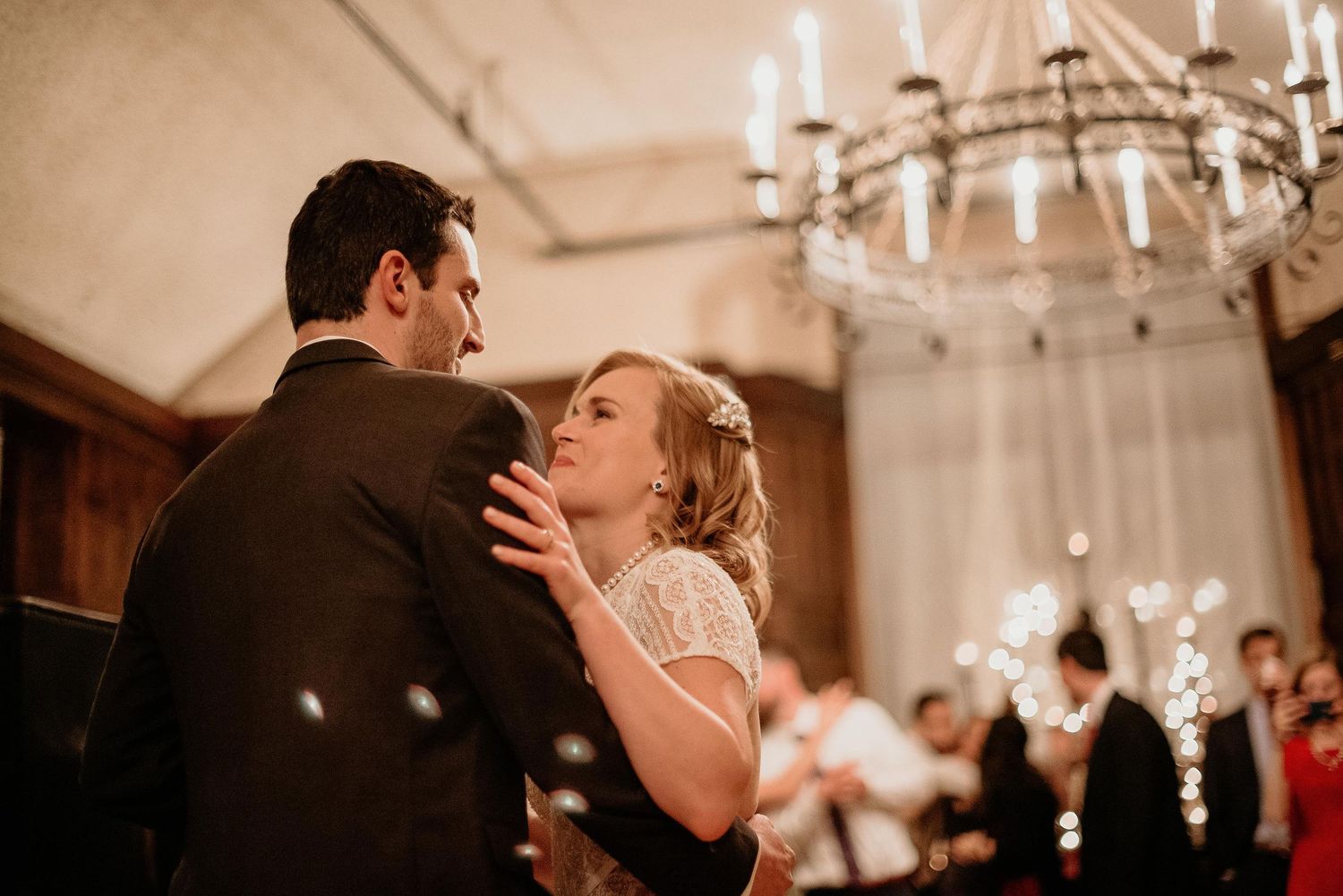 Couple sharing their first dance at elegant wedding reception under chandelier with sparklers.