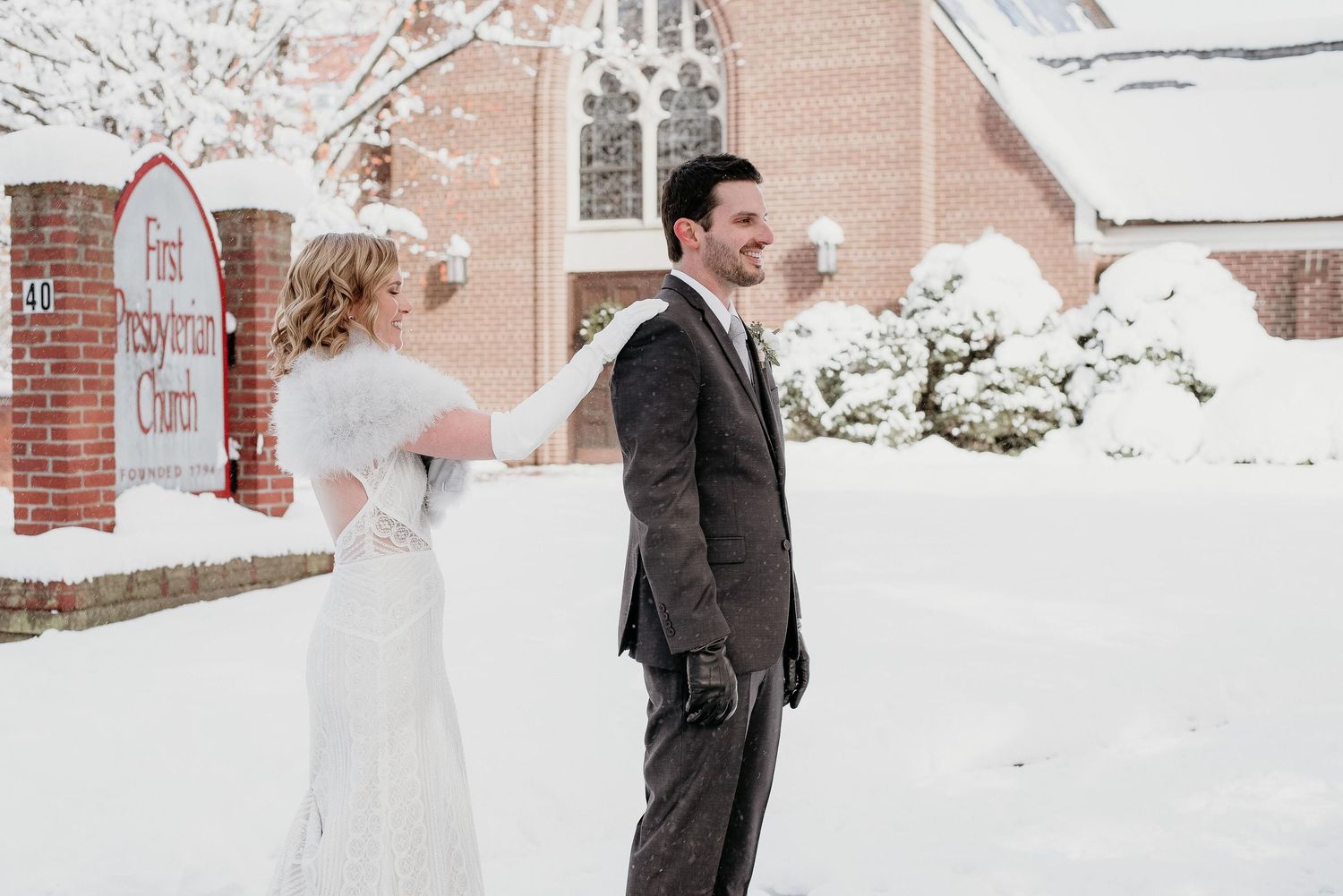 Bride and groom share a joyful moment outside a snow-covered First Presbyterian Church on their winter wedding day.