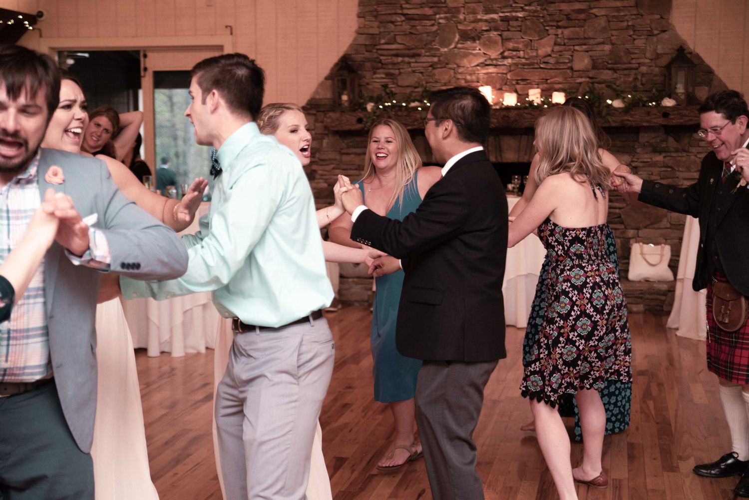 Guests dancing joyfully at an elegant wedding reception in a rustic stone venue with warm lighting.