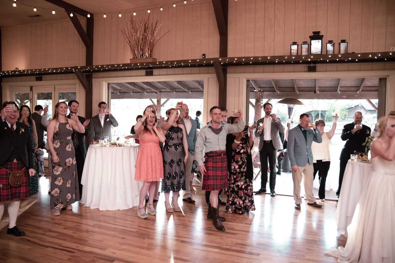 Wedding guests in kilts and formal attire dancing and celebrating at a rustic barn reception venue.