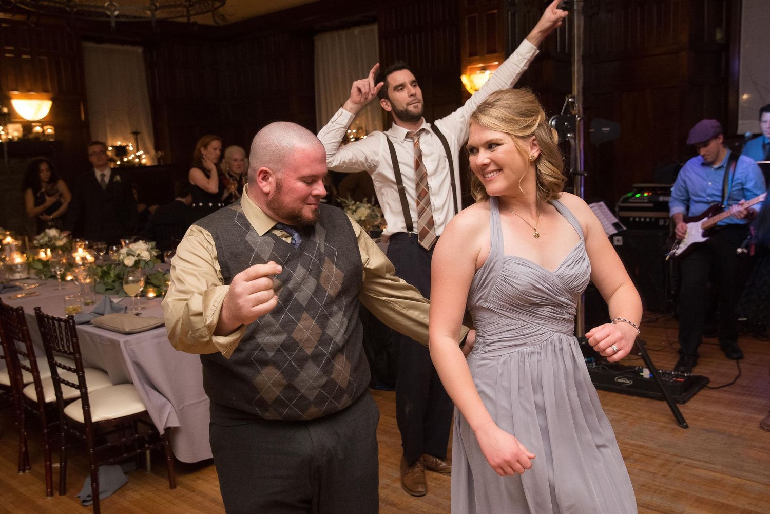 Guests dancing joyfully at a wedding reception in an elegant banquet hall with warm lighting.