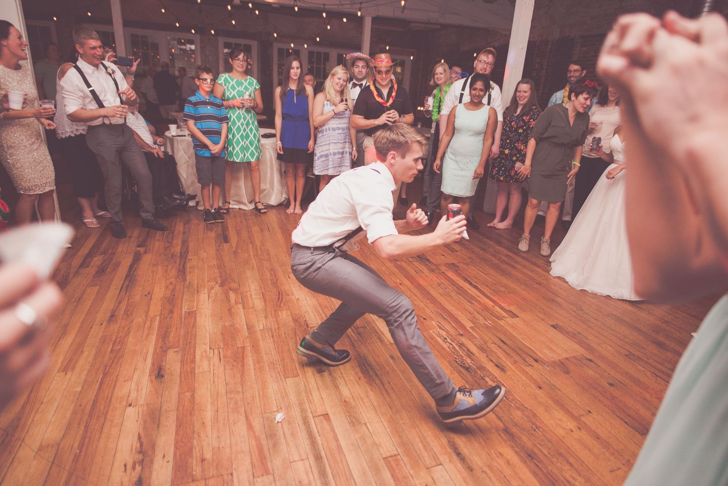Guest performing energetic dance moves on wooden dance floor at wedding reception.