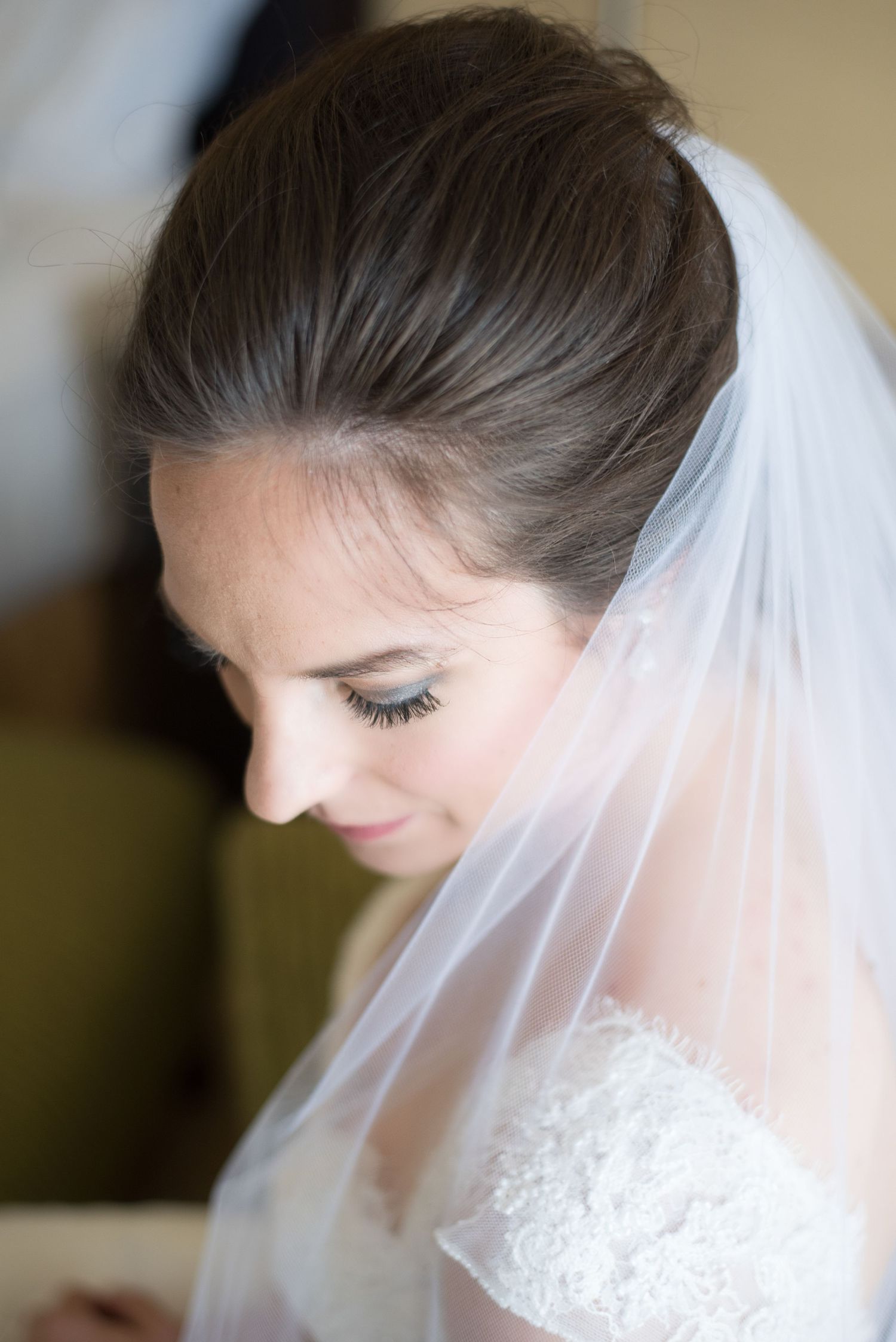 Close-up portrait of brunette bride wearing lace dress and sheer veil looking down gracefully.