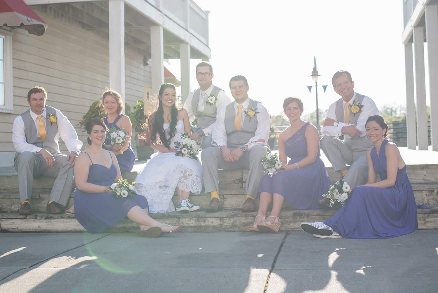 Wedding party in navy and gray poses casually on outdoor steps in bright sunny weather.