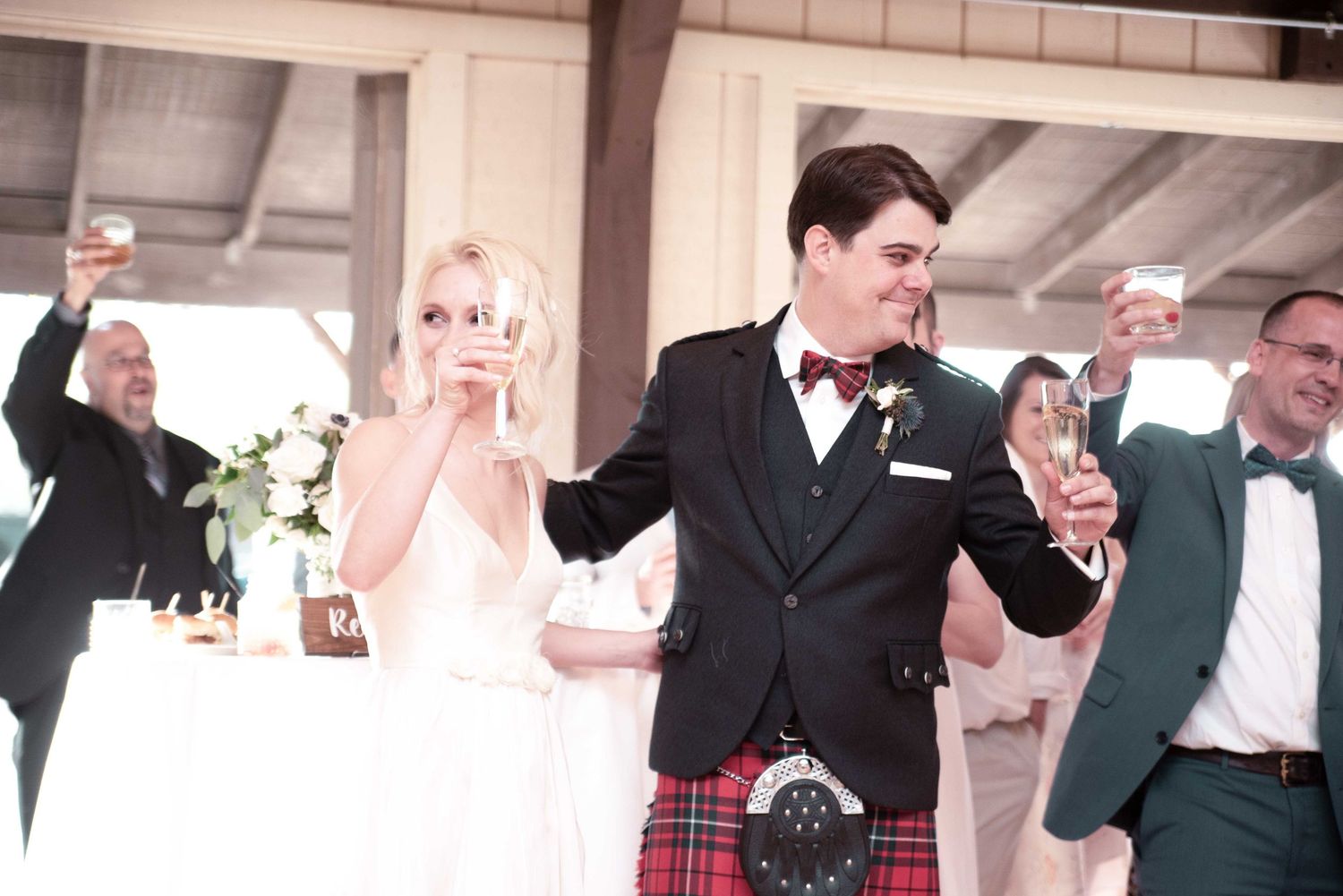 Bride and groom in Scottish kilt toasting with guests at elegant wedding reception.