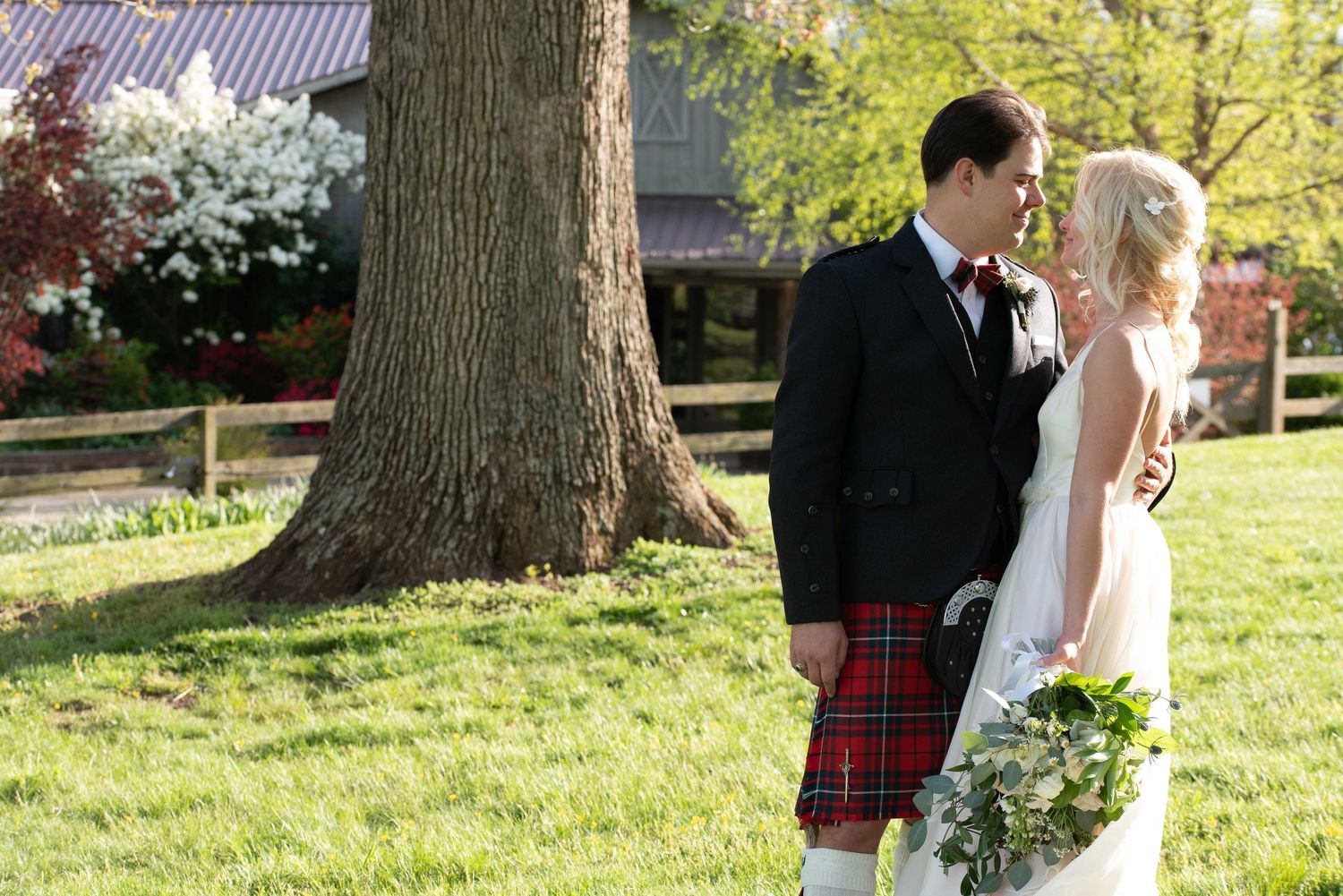 Bride and groom share a romantic moment outdoors, groom wearing a traditional Scottish tartan kilt at a wedding.