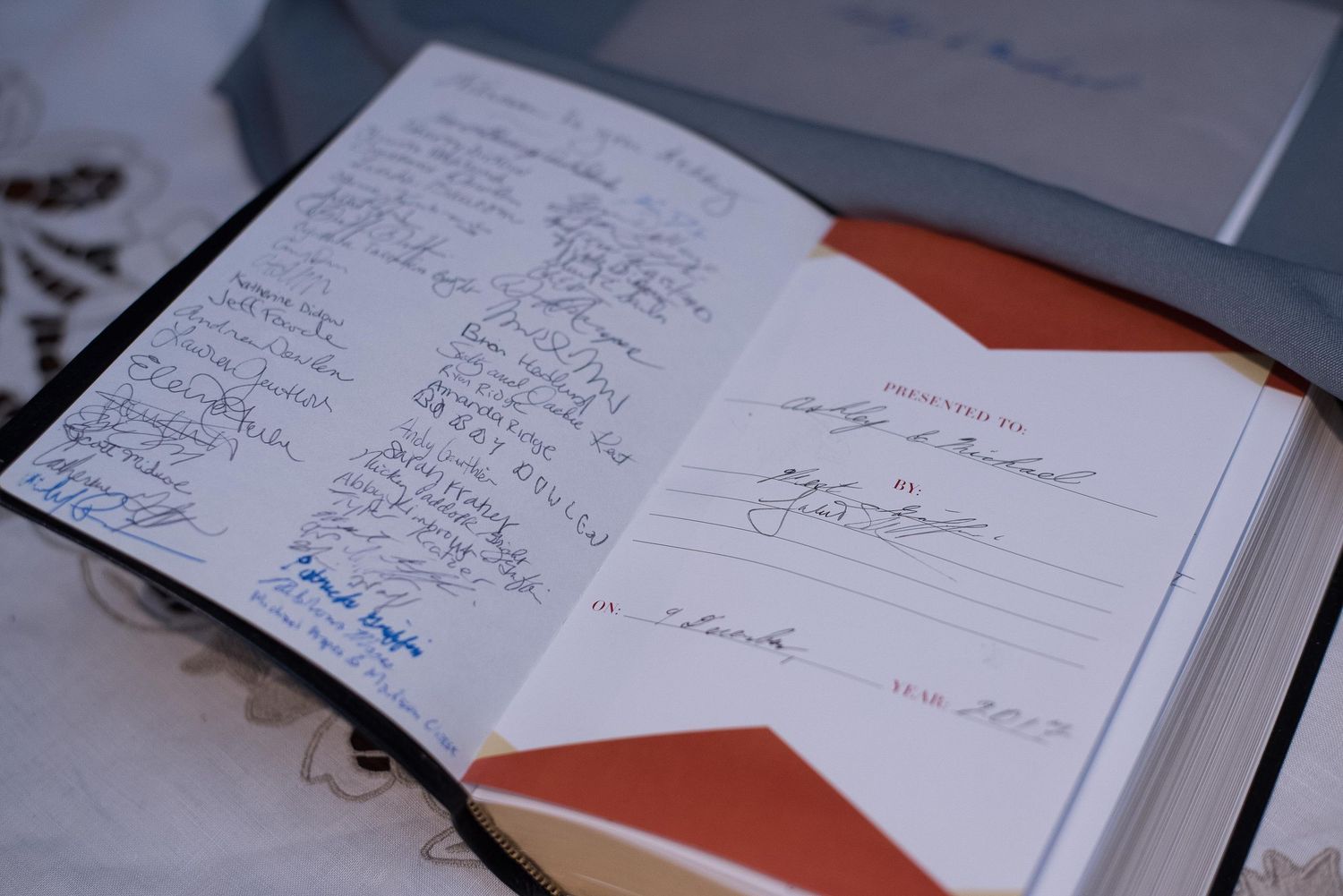 Open guest book with signatures and handwritten notes, featuring a red and gold cover with a formal dedication page.