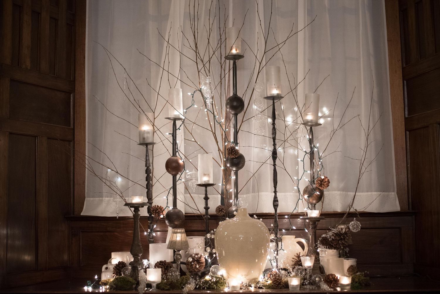 Elegant winter centerpiece with tall candlesticks, bare branches, ornaments, and glowing candles on a decorated table.