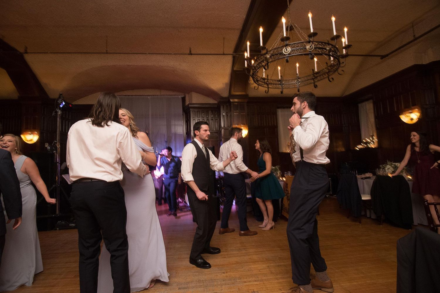 Guests dancing at an elegant wedding reception in a dimly lit ballroom with chandelier lighting.