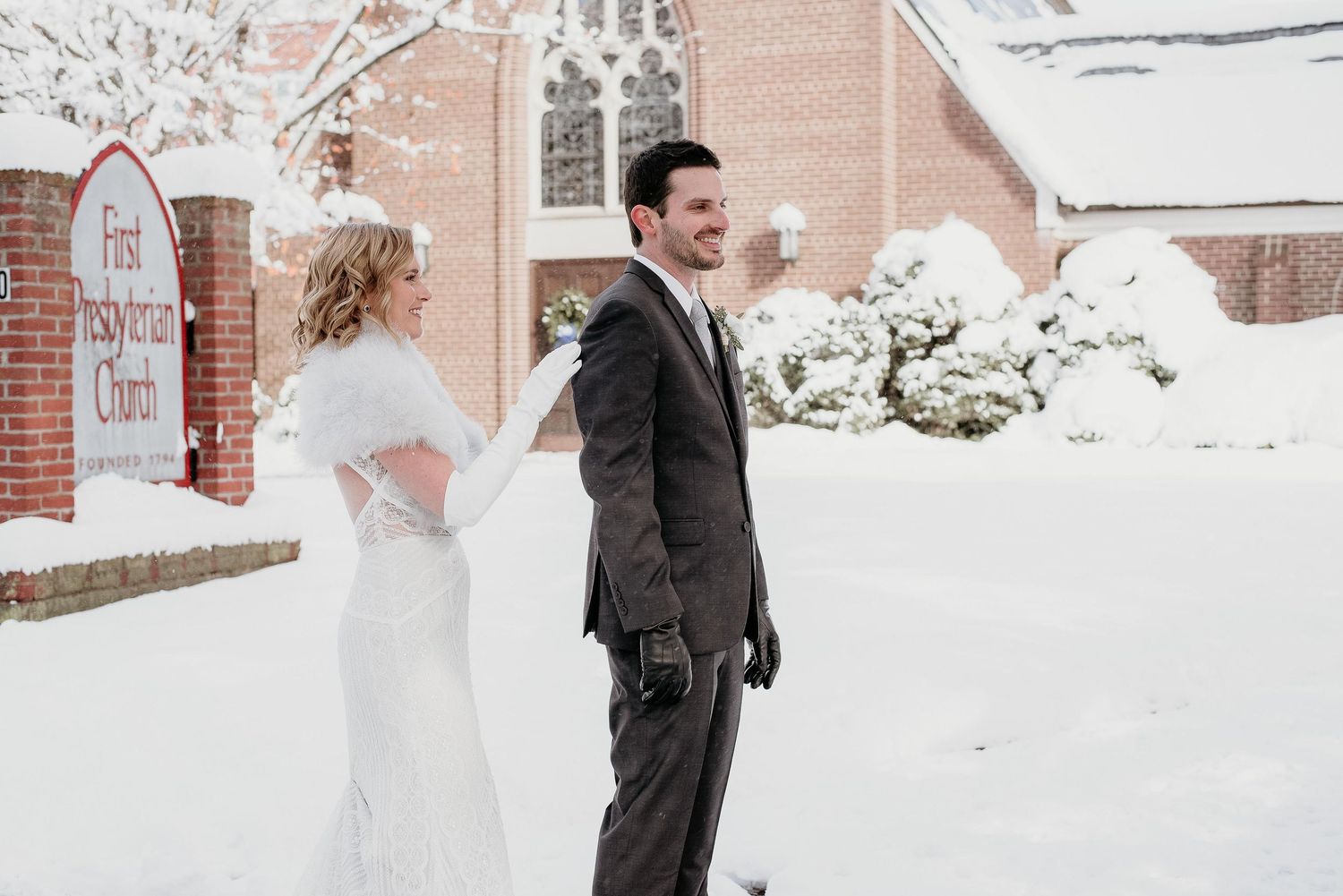 Bride and groom share a joyful moment outside a snow-covered First Presbyterian Church on their winter wedding day.