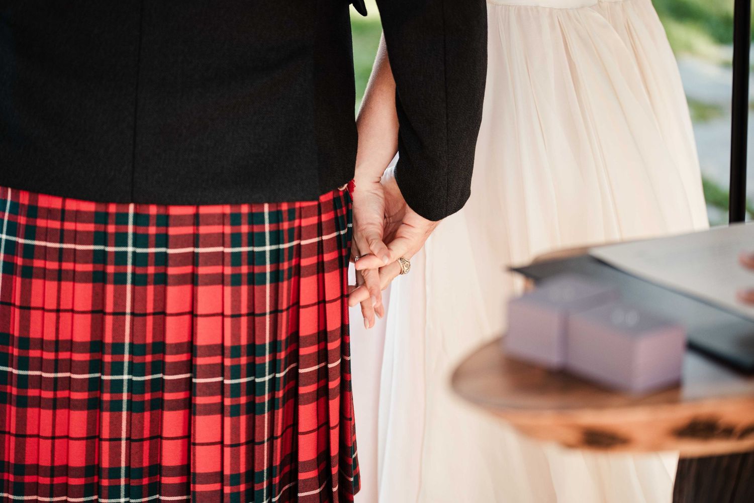 Couple holding hands, groom wearing red tartan kilt and bride in white dress at wedding ceremony.