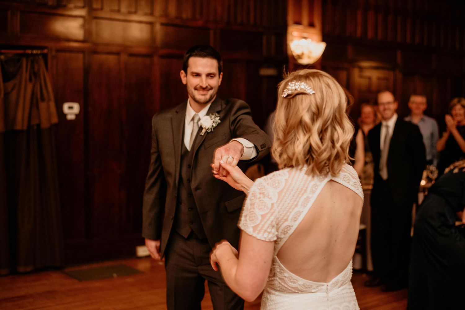 Bride and groom share their first dance in an elegant wood-paneled ballroom during their wedding reception.