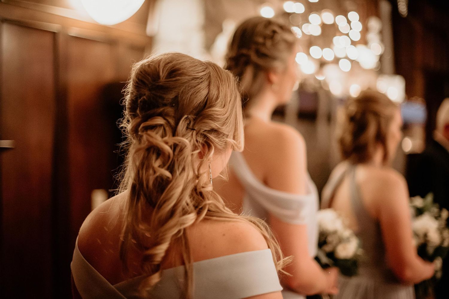 Bridesmaids with elegant braided updo hairstyles wearing off-shoulder dresses at a rustic wedding venue.
