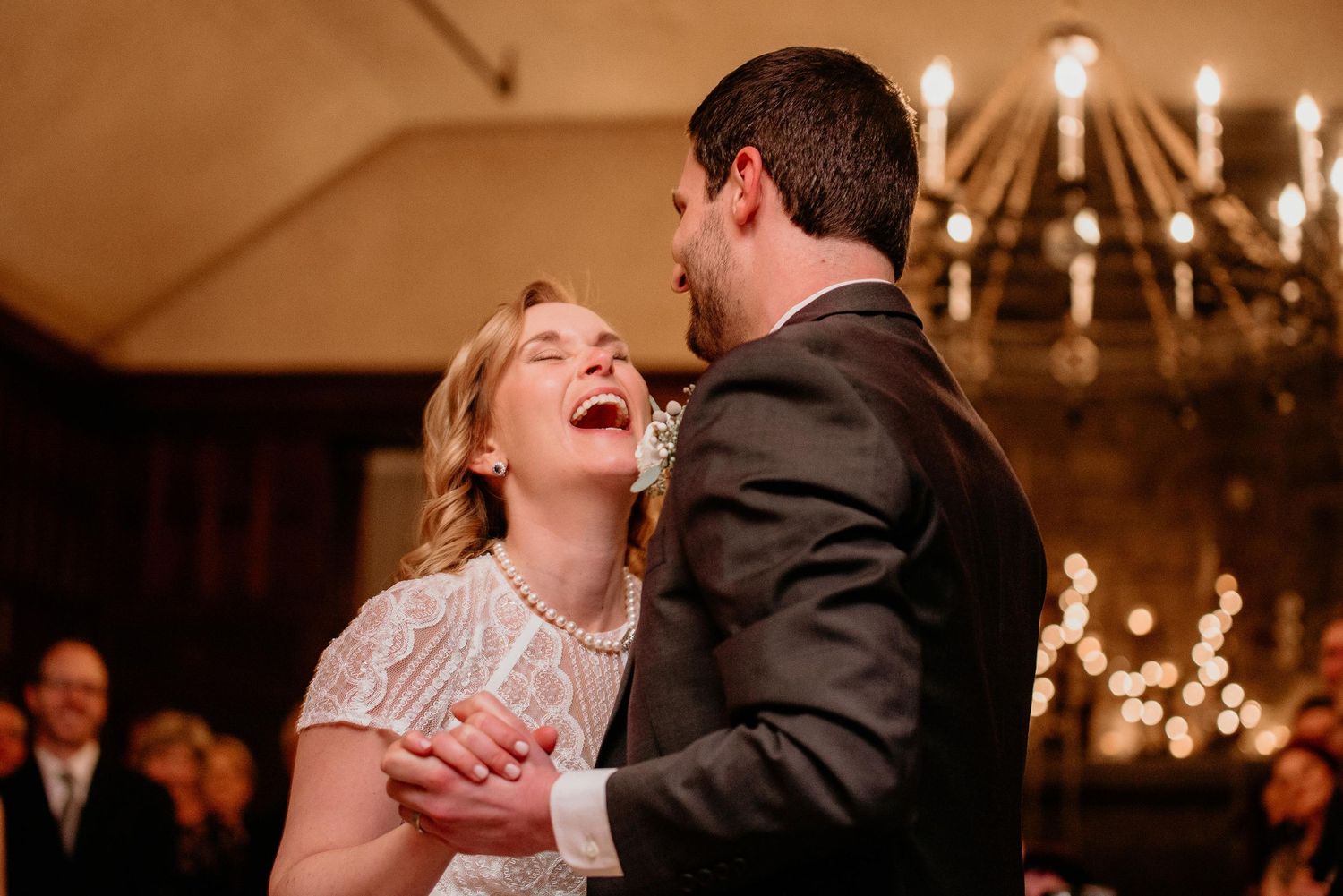 Bride laughing joyfully with groom during first dance at elegant candlelit wedding reception.