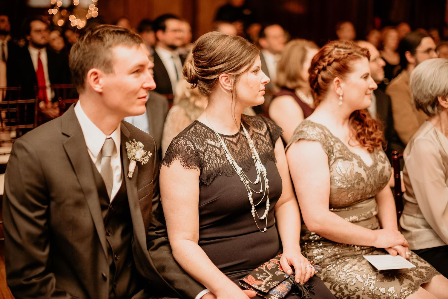 Guests in formal attire seated at an elegant wedding ceremony, smiling and enjoying the celebration.