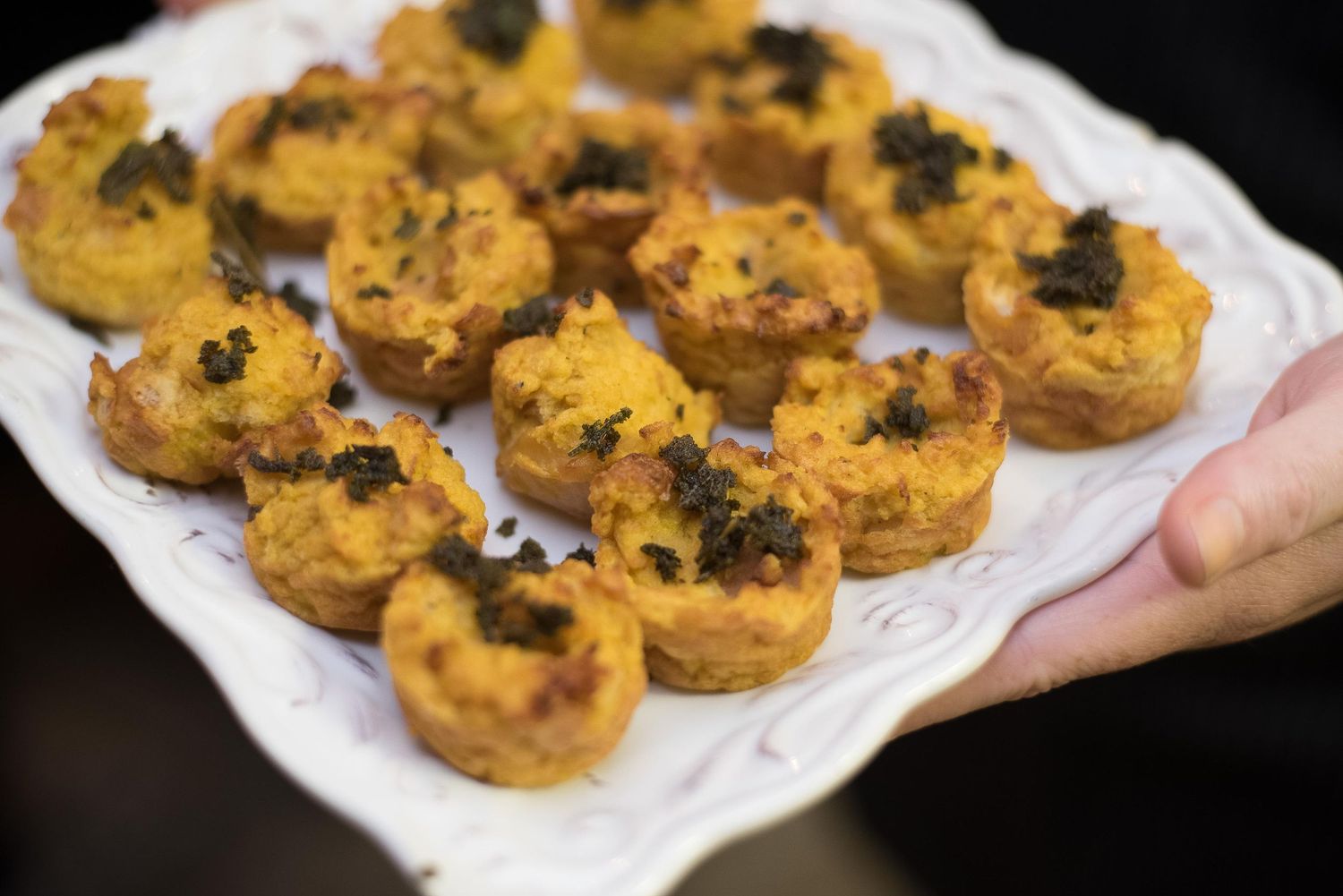 Golden mini quiche bites topped with black caviar served on a white decorative platter at a catered event.
