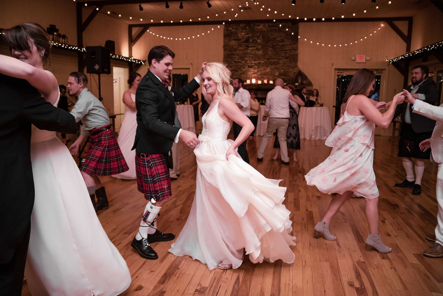 Bride and groom dancing joyfully with guests at a rustic wedding reception venue.
