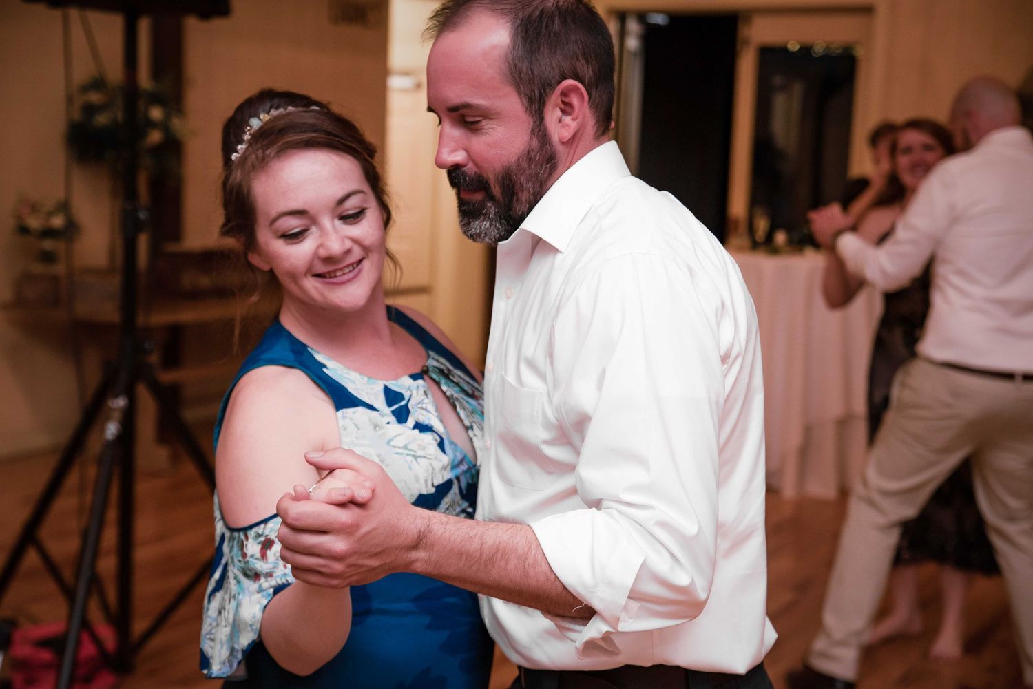 Couple dancing together at a wedding reception, woman in blue dress smiling, man in white shirt, elegant venue.