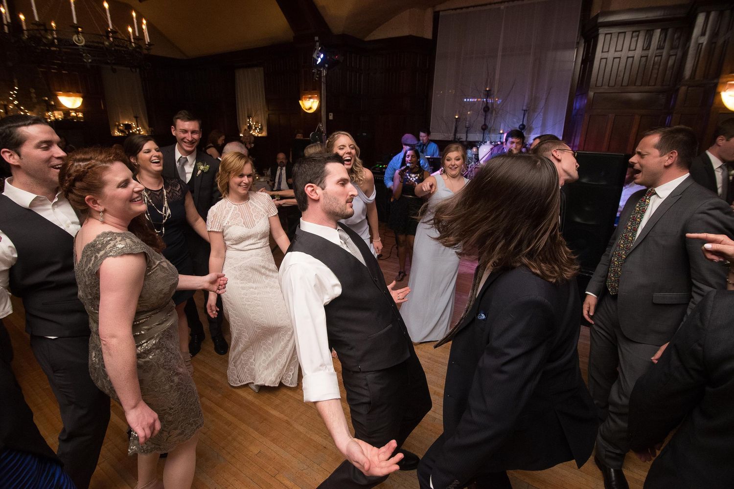 Wedding guests dancing joyfully at a elegant indoor reception venue with chandeliers and warm lighting.