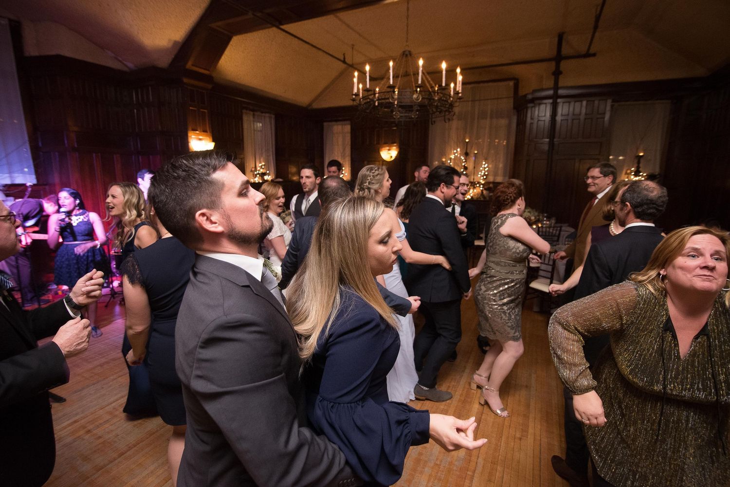 Guests dancing and socializing at an elegant indoor wedding reception with chandeliers and warm lighting.