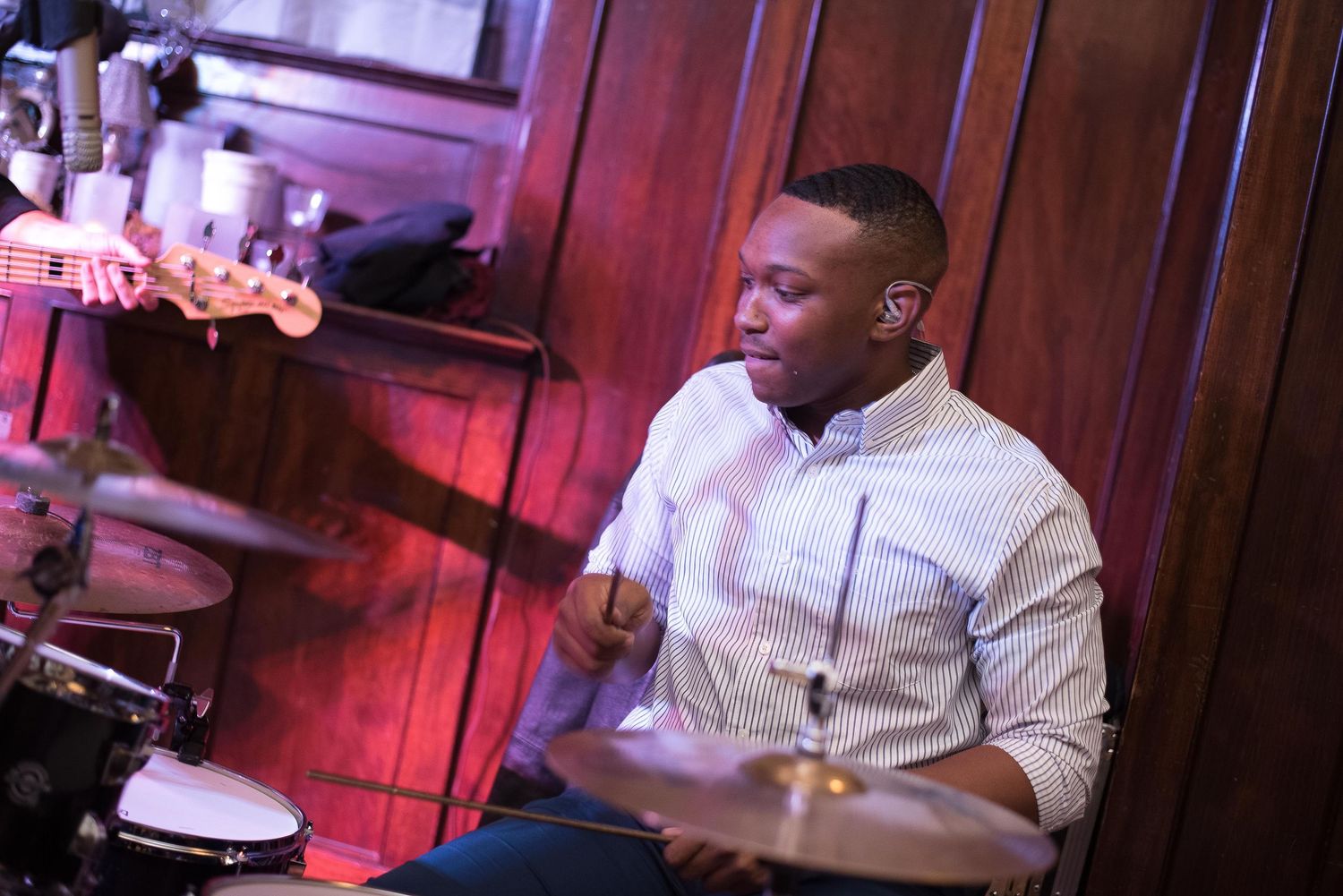 Young man playing drums on stage at a live music venue with warm lighting.