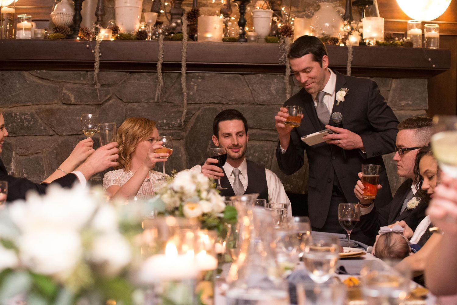 Wedding guests raising glasses during a heartfelt toast at an elegant candlelit reception dinner.