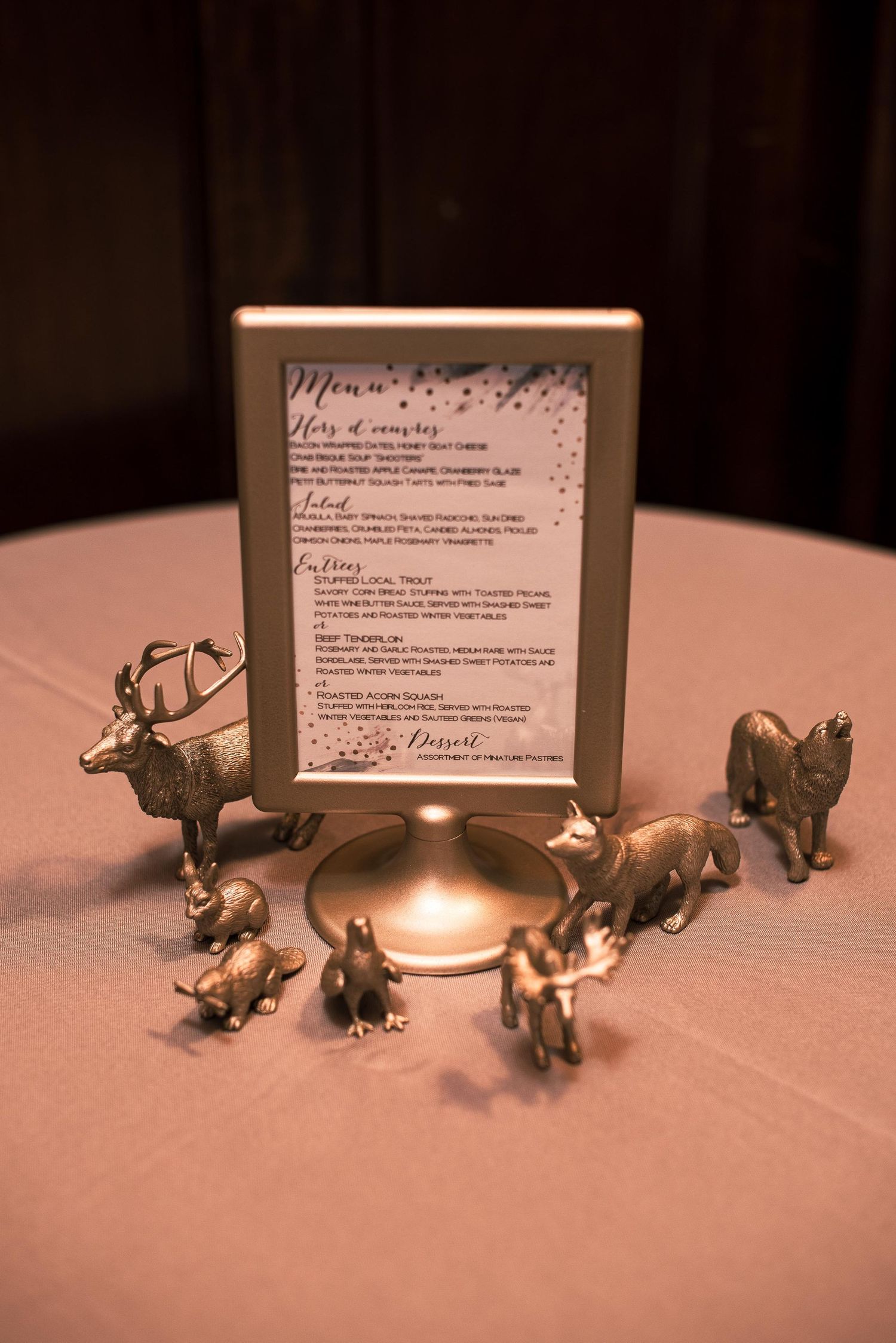 Gold animal figurines surround a framed wedding menu card on a pink tablecloth at an elegant reception.