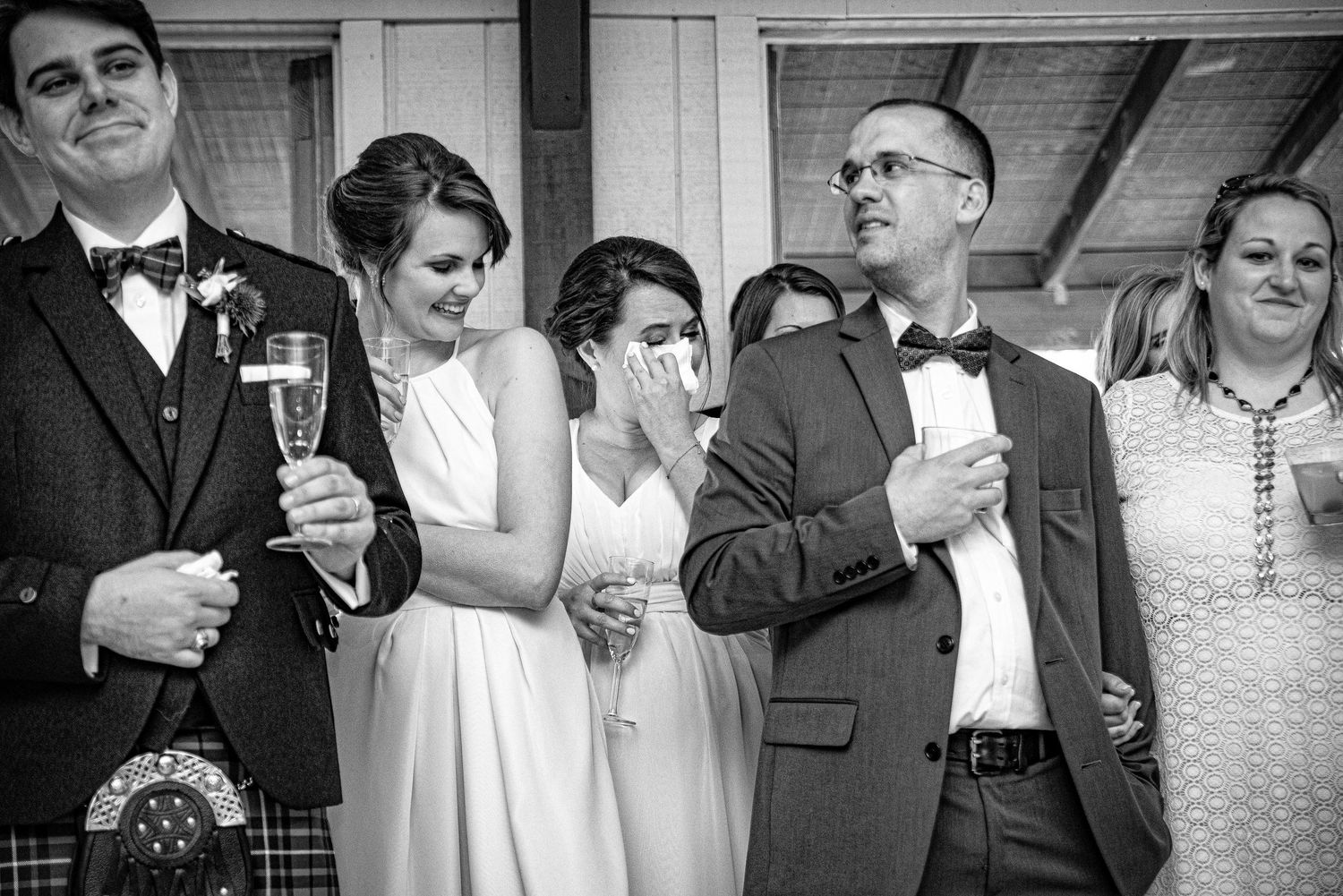 Black and white wedding photo of emotional guests laughing and crying during speeches at a reception.