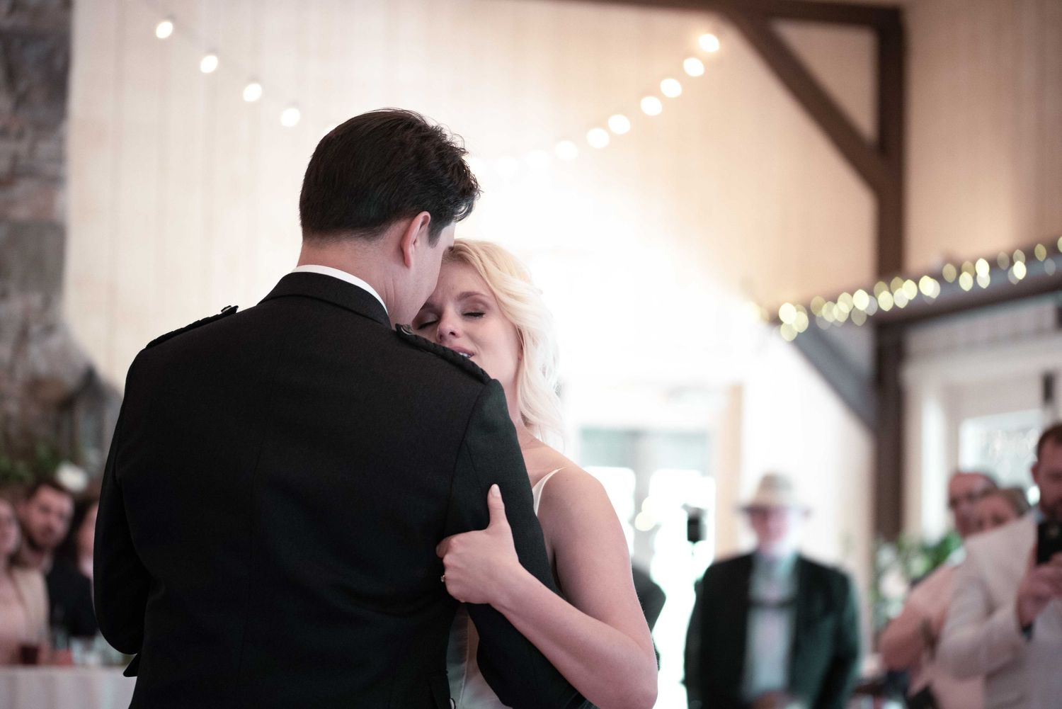 Bride and groom share their first dance in a warmly lit barn wedding venue with string lights.