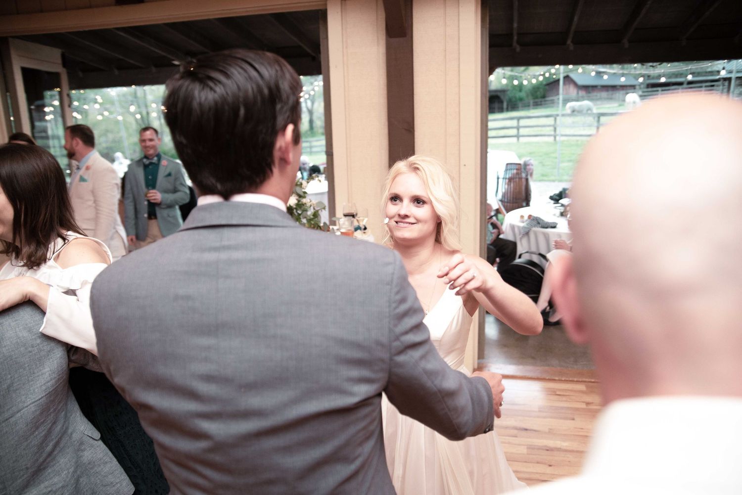 Smiling blonde woman in white dress dancing with man in gray suit at elegant wedding reception.